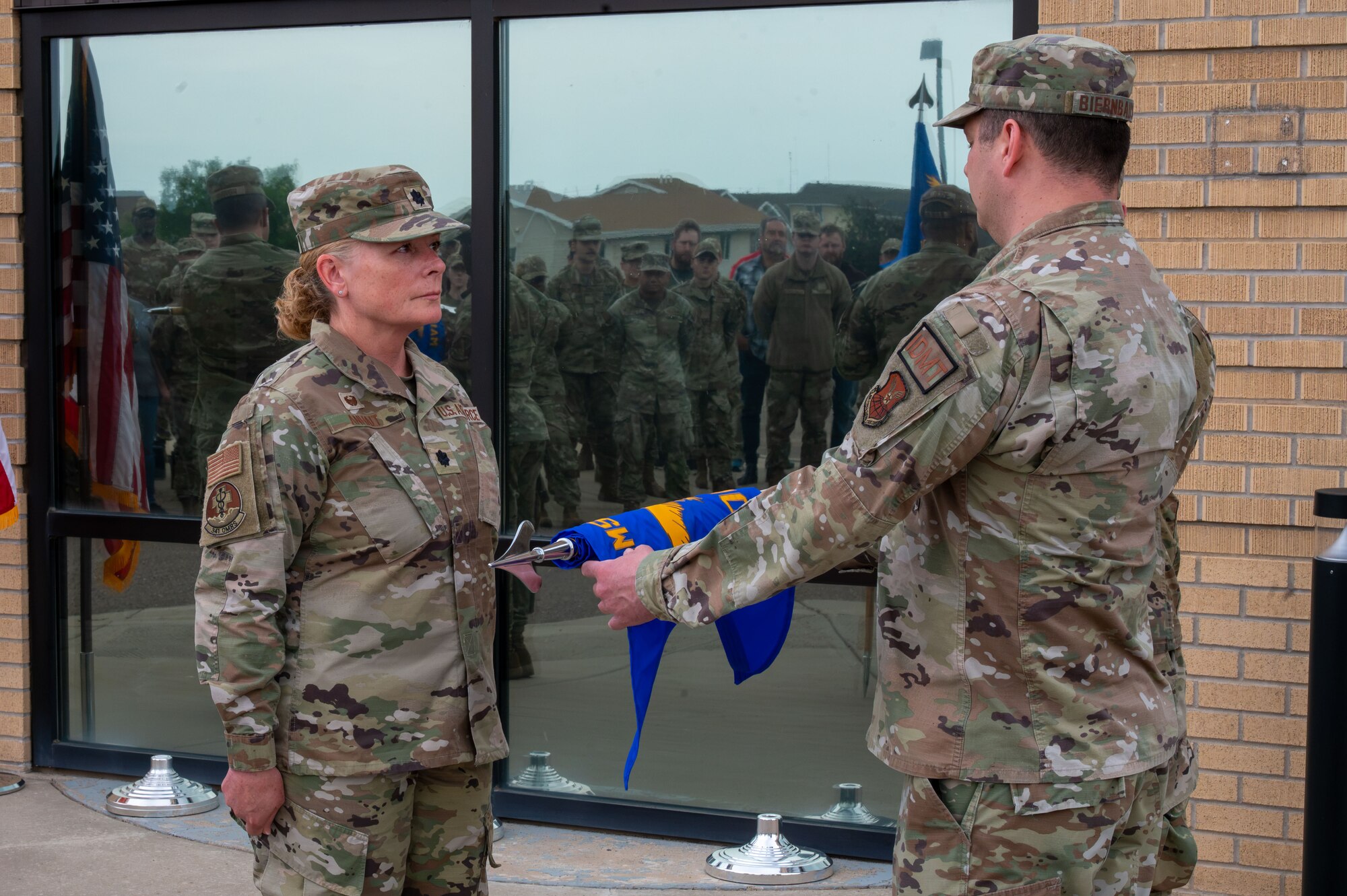 U.S. Air Force Lt. Col. Melissa Anhalt, Malmstrom Operational Medical Readiness Squadron commander, left, and Master Sgt. Brett Biernbaum, Malmstrom OMRS flight chief, unfurl the new Operational Medical Readiness Squadron guidon during the Air Force Medical Command’s fourth inter-command transfer, at Malmstrom Air Force Base, Montana, June 26, 2026.