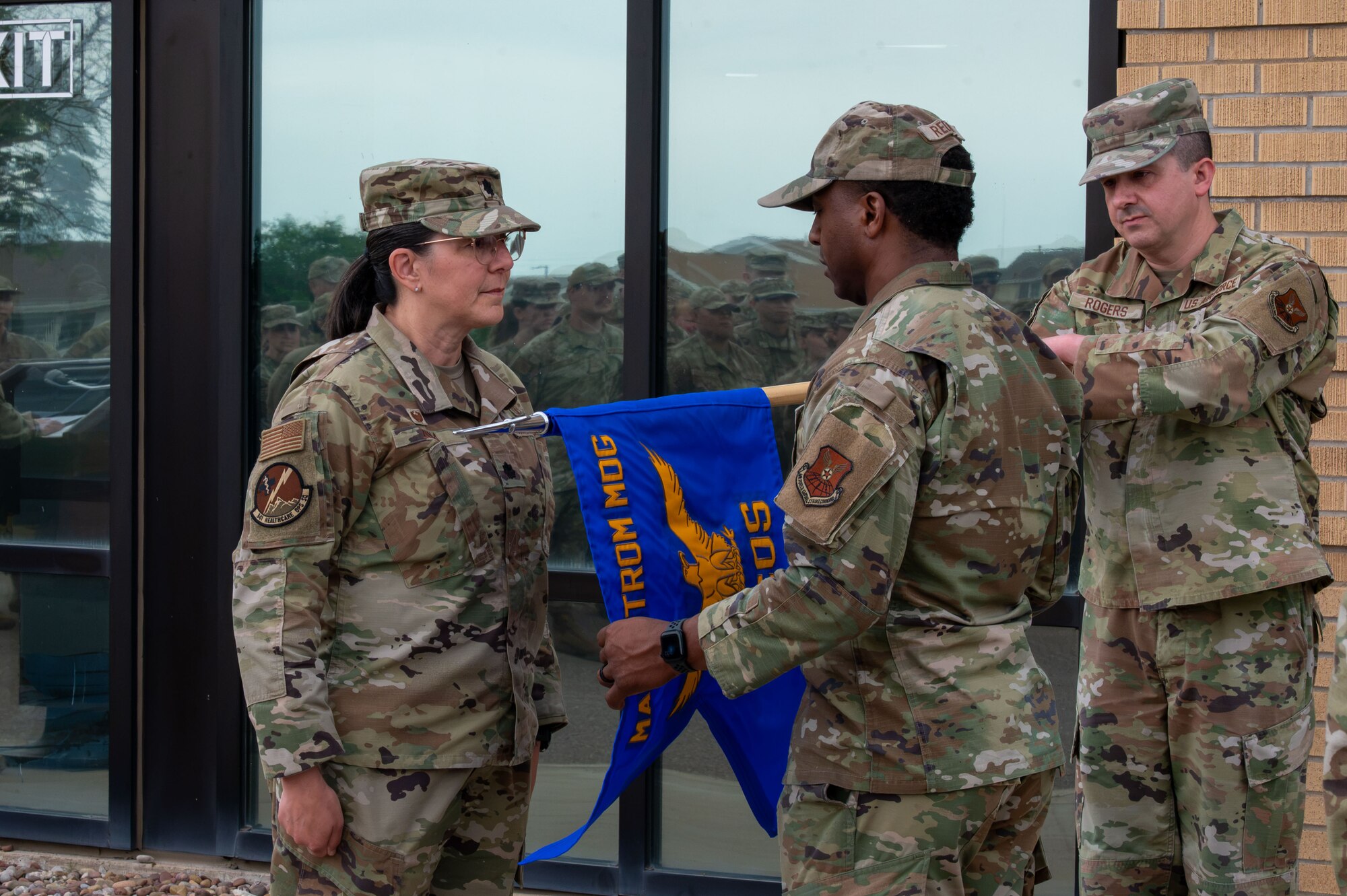 U.S. Air Force Lt. Col. Denise Zona, Malmstrom Healthcare Operations Squadron commander, left, and Master Sgt. Covito Redman, Malmstrom Healthcare Operations Squadron senior enlisted leader, unfurl the new Healthcare Operations Squadron guidon during the Air Force Medical Command’s fourth inter-command transfer, at Malmstrom Air Force Base, Montana, June 26, 2026.