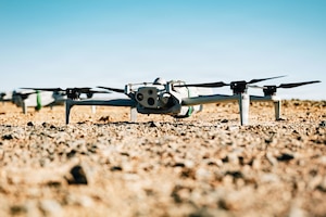 A drone sits on the ground during daytime, with another drone in the background.