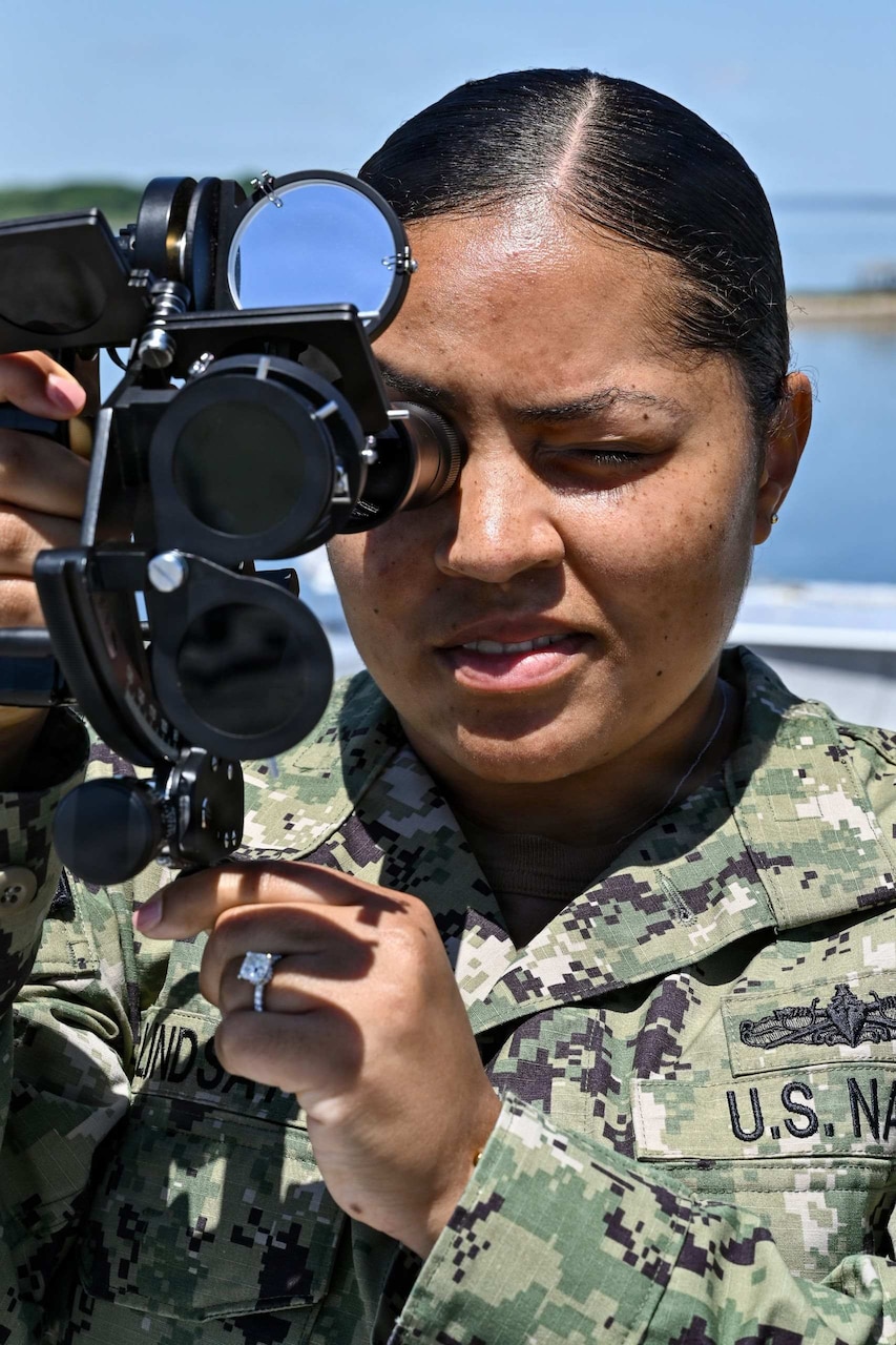 A woman wearing a camouflage military uniform peers into a military ocular device.