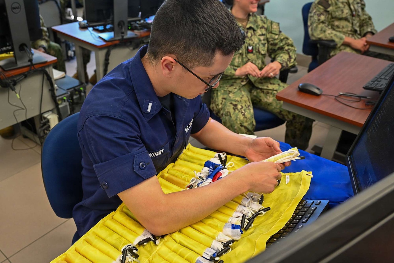 A man, wearing a blue Navy uniform, pulls a small rolled up flag out of a yellow flag holder.