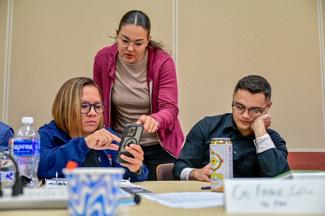 Three people are gathered around a table looking at a phone