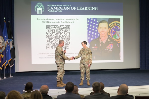 Two Army soldiers shake hands on a stage.