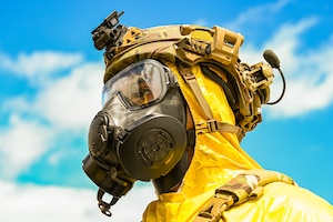 photo of an Airman in a yellow hazmat suit with a gas mask on