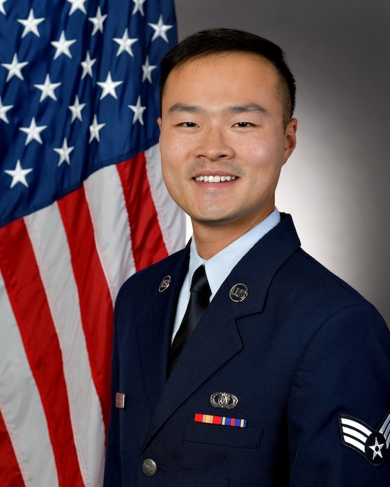 An airman in uniform poses in front of the U.S. flag