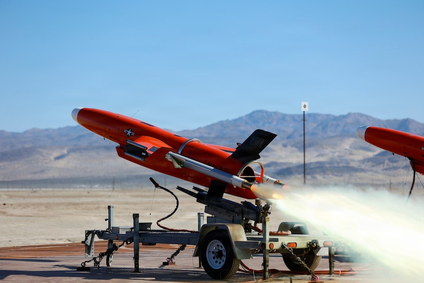 A missile launches from a trailer in the desert as smoke pours out the back; there are mountains in the background.