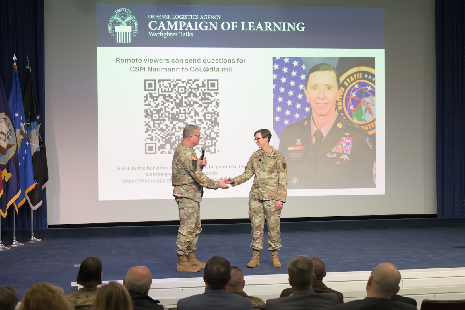 Two Army soldiers shake hands on a stage.
