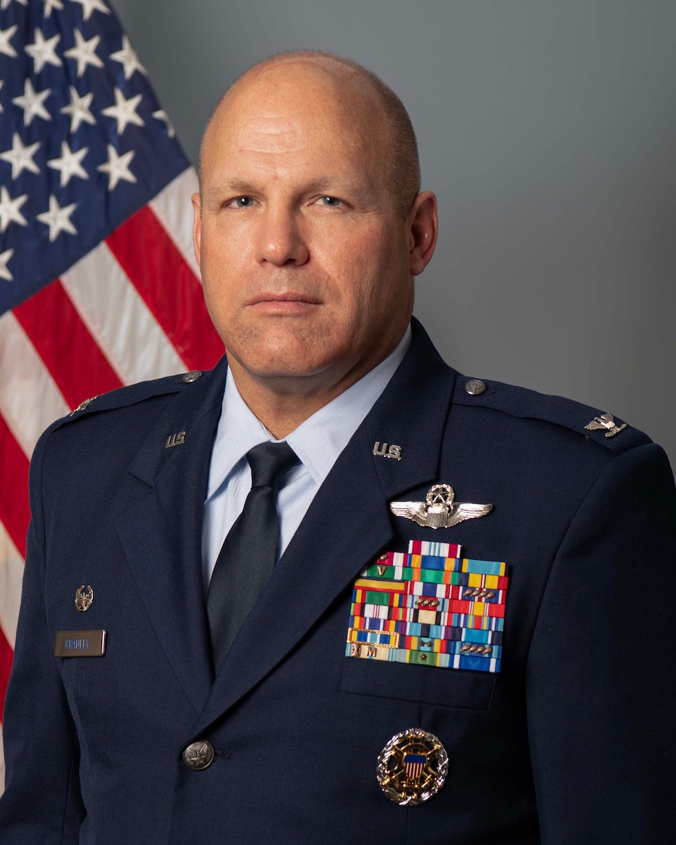 Male officer standing in front of USA flag wearing blue uniform.