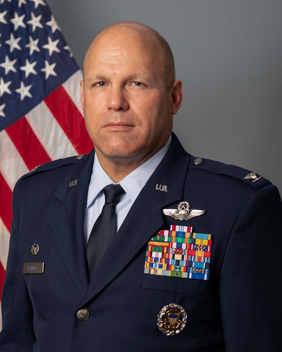 Male officer standing in front of USA flag wearing blue uniform.