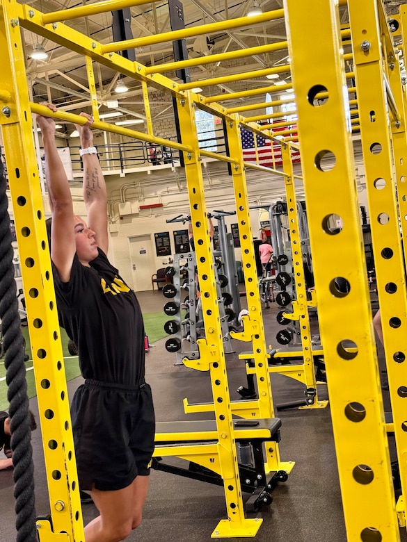 A woman hangs from yellow strength training bars.