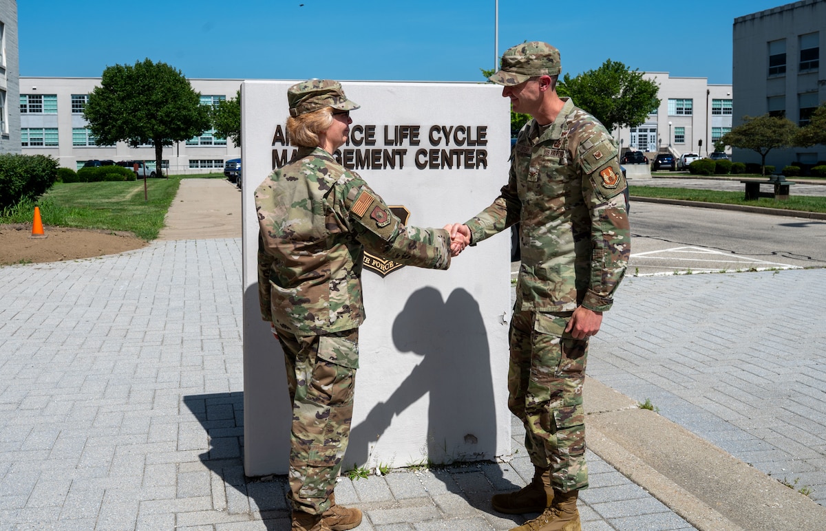 Two Air Force service members shake hands outside in front of a sign.