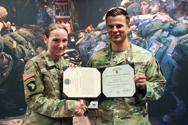 People wearing camouflage military uniforms stand inside a holding a certificate.