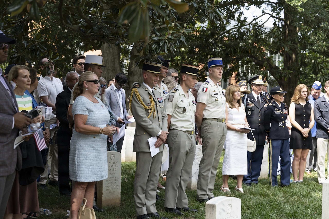Dozens of people in formal attire stand outside during a ceremony.