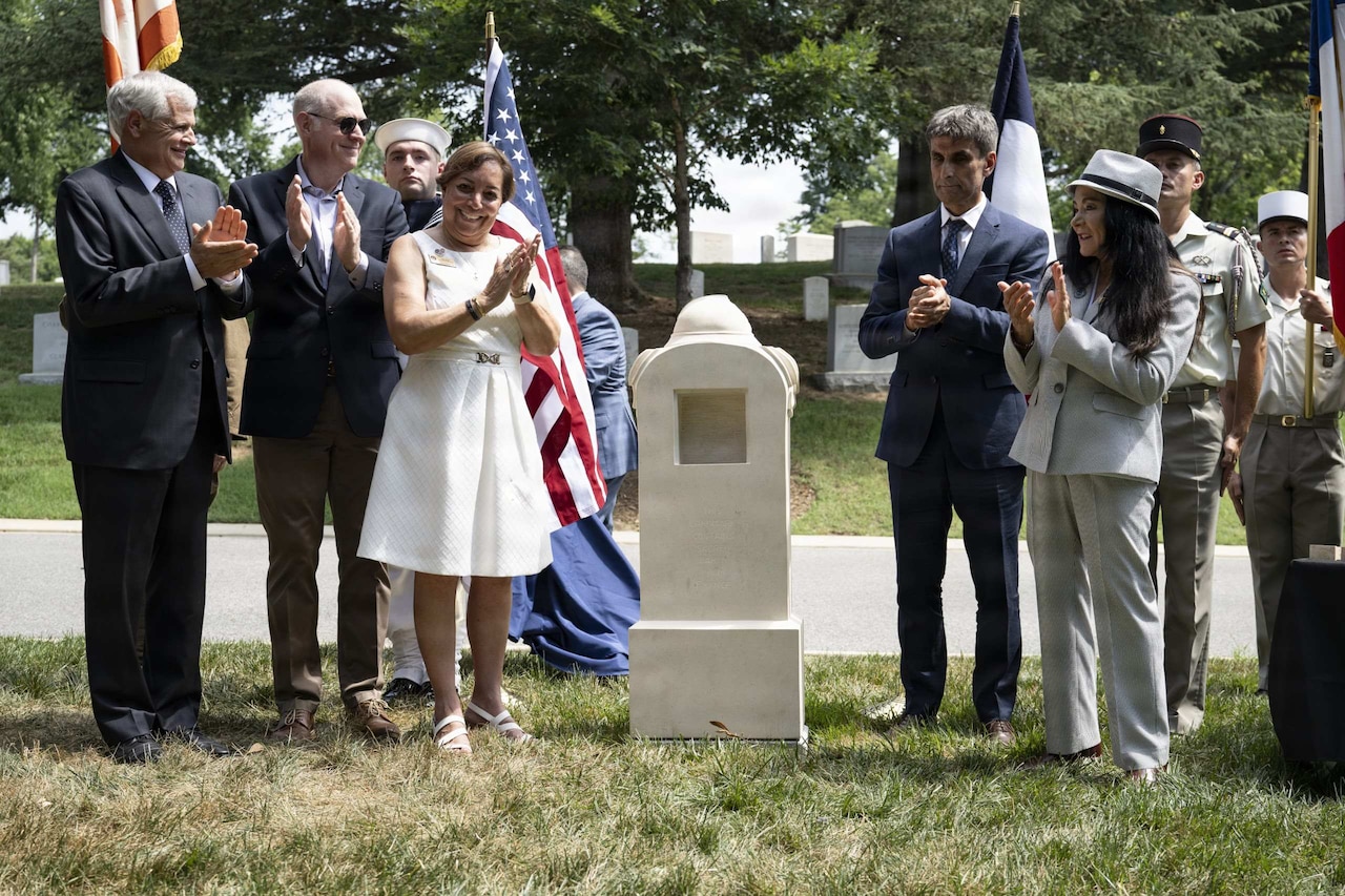 A group of people in formal attire clap after the unveiling of a monument.