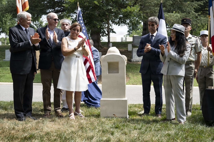 A group of people in formal attire clap after the unveiling of a monument.