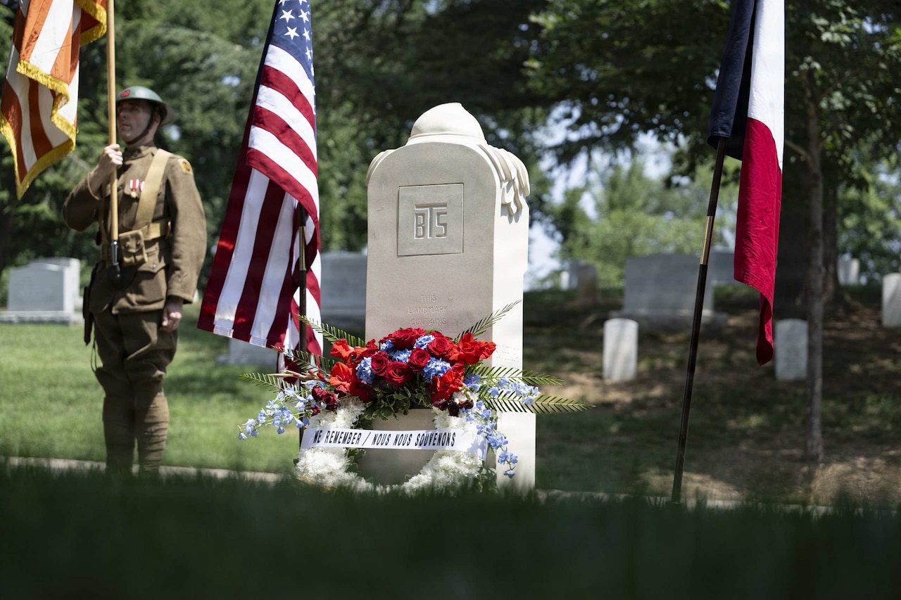 A wreath is displayed in front of a monument at a cemetery with the American and French flags hanging on the sides of the monument.