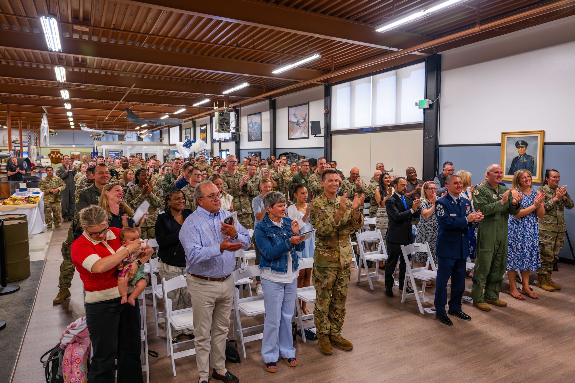 A large crowd stands and applauds during a ceremony indoors.