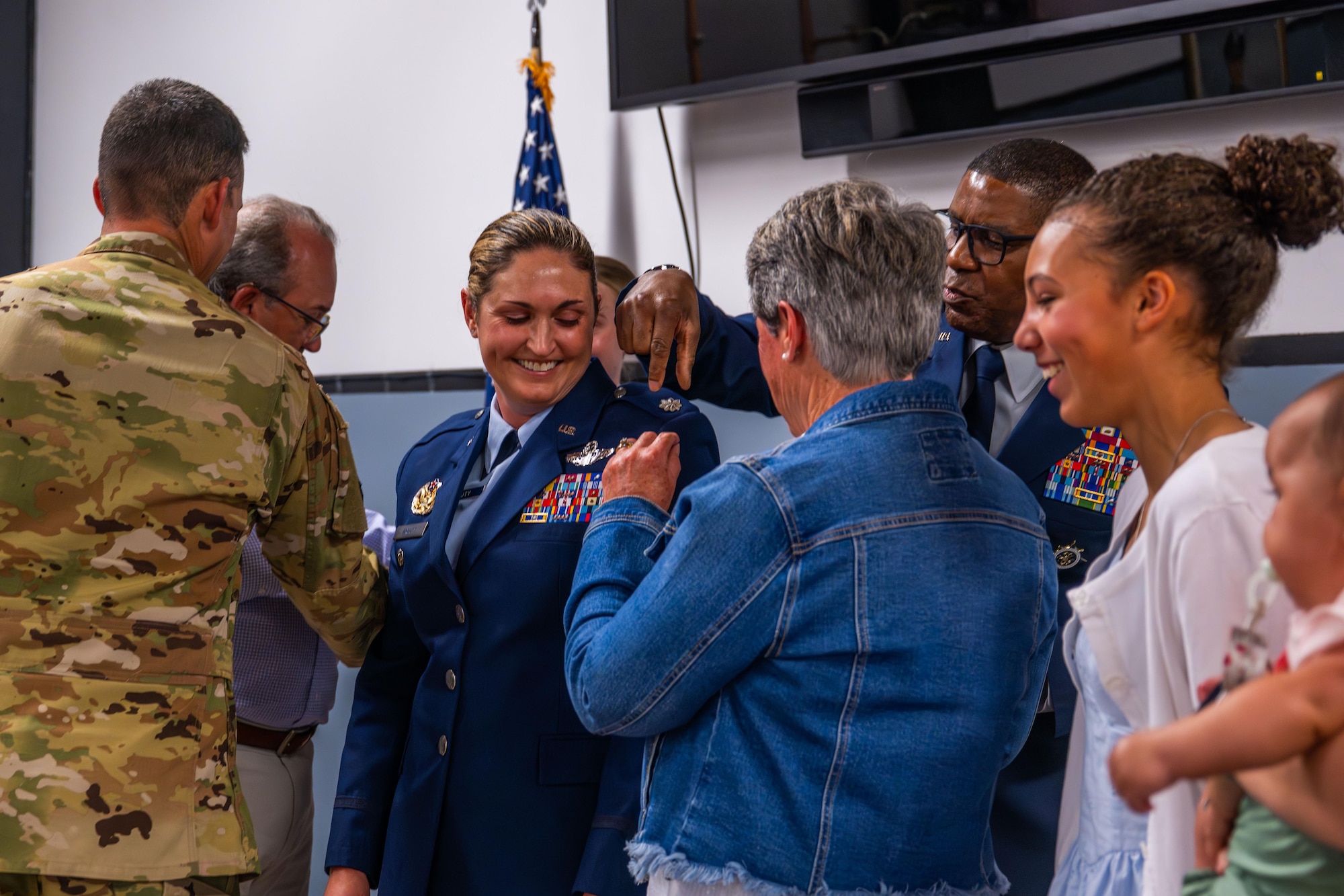 A military colonel smiles as family and friends help pin her new rank onto her uniform.