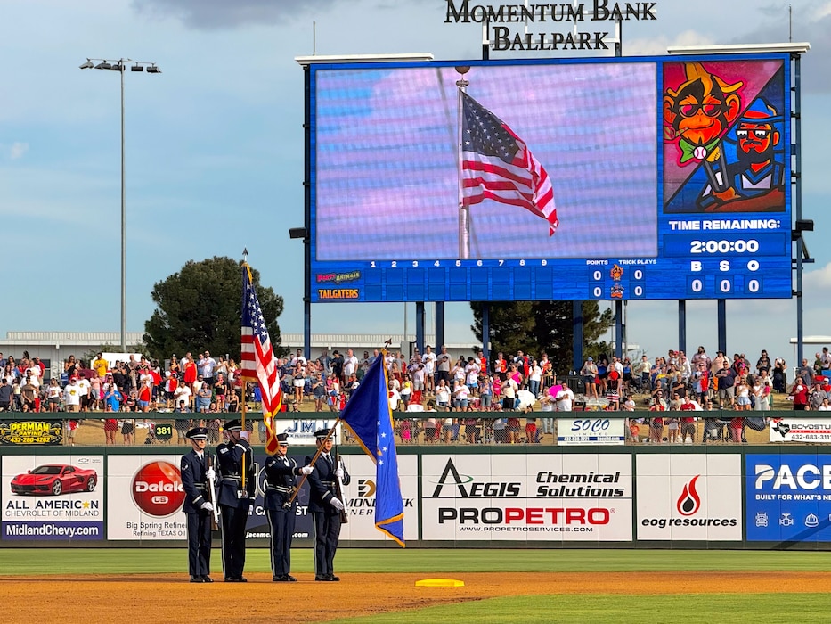 Base Honor Guard members are wearing their blue presenting the colors center field at a baseball game