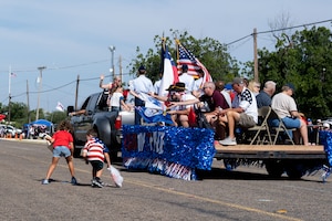 A parade float passes on a road and kids are picking up candy being tossed by participants on the float