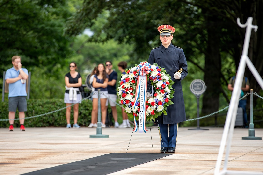 A Tomb Guard in dress uniform stands at attention behind a large ceremonial flower wreath at the Tomb of the Unknown Soldier