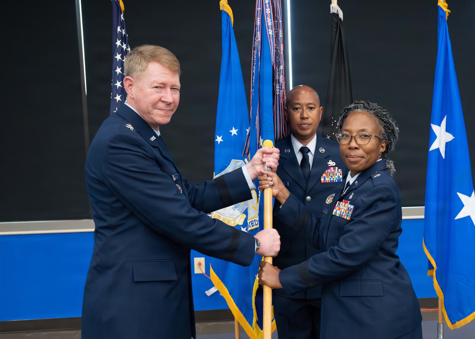 Brig. Gen. Gwendolyn A. Foster (right), relinquishes the guidon to Maj. Gen. (Dr.) Robert K. Bogart is the Director, Defense Health Network Central, and Commander, Medical Readiness Command Alpha (left) at the 59th MDW change of command ceremony at Joint Base San Antonio-Lackland on July 8, 2026.