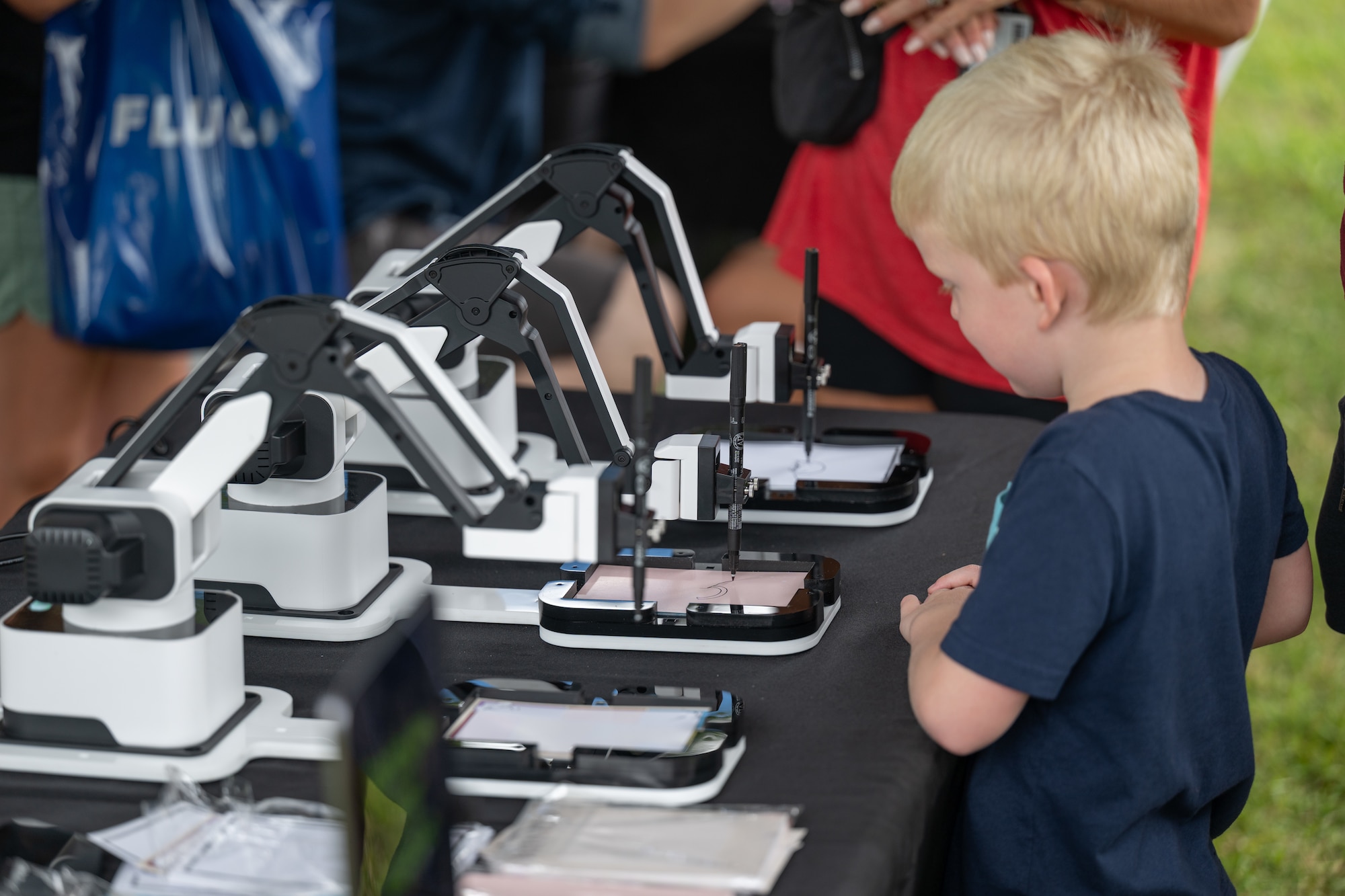 A young attendee watches as robots complete programmed drawings June 27, 2026, during the Arnold Engineering Development Complex 75th anniversary open house event at Arnold Air Force Base, Tenn., headquarters of AEDC. The event included a children’s “Fun Zone” that featured inflatables, trampolines and a petting zoo, as well as a STEM area where attendees could learn about science and technology. (U.S. Air Force photo by Keith Thornburgh)