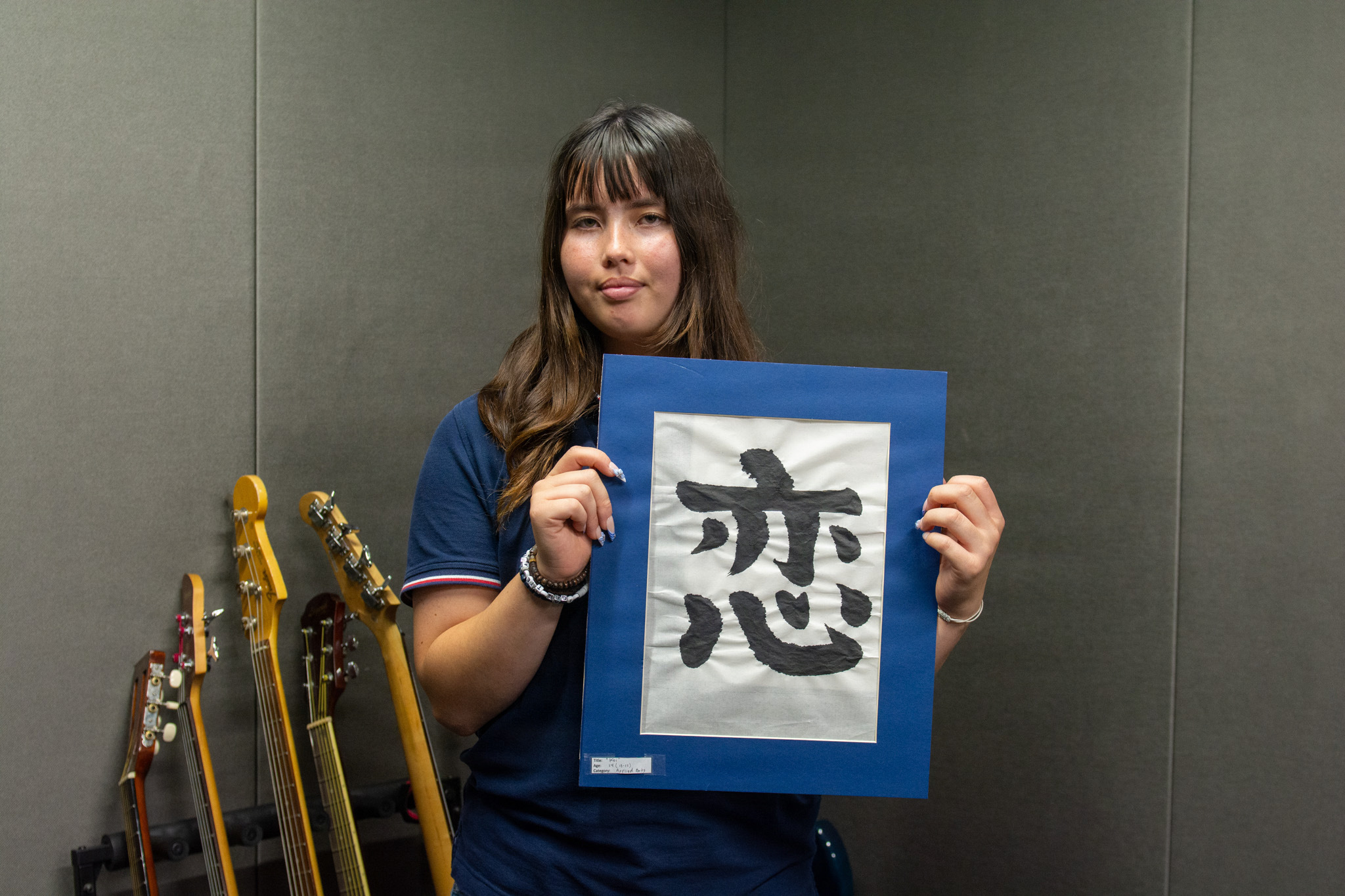 Riley M. holds her award-winning artwork, "Koi" at the Commander, Fleet Activities Works Yokosuka Teen Center June 9, 2026. Her piece, created using traditional Japanese calligraphy, earned national recognition in the Boys & Girls Clubs of America’s 2025-26 National Arts Contest