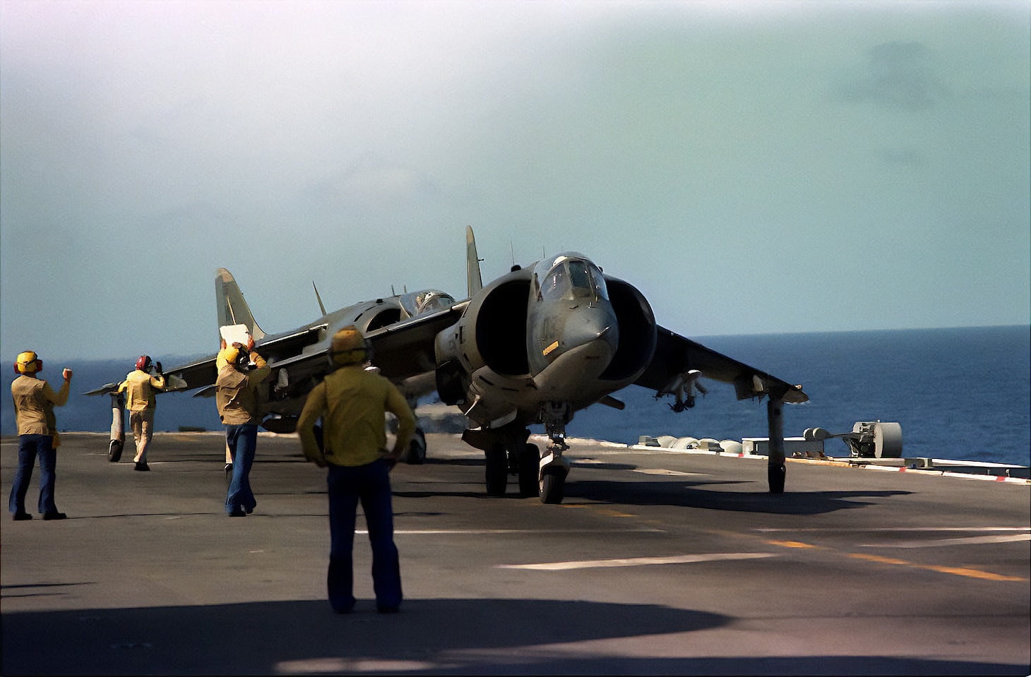 Flight deck crewmen reposition AV-8C Harrier aircraft on the flight deck of the amphibious assault ship Guadalcanal (LPH 7) during Exercise AHUAS TARA II, taking place off the coast of Honduras during 1983.