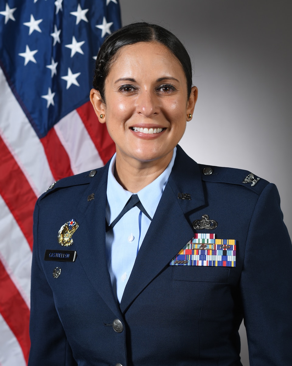 Photo is a headshot of a woman in uniform in front of flag