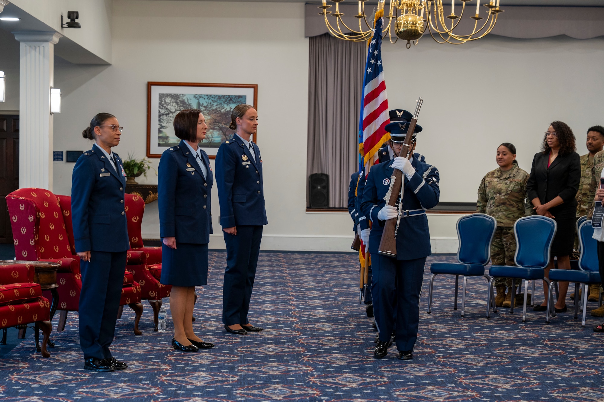 A photo of an Air Force Col., Maj. and Lt. Col. standing at attention while the Honor guard post the colors.