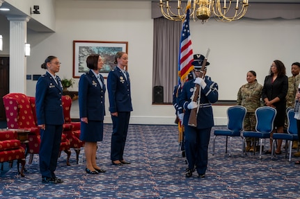 A photo of an Air Force Col., Maj. and Lt. Col. standing at attention while the Honor guard post the colors.