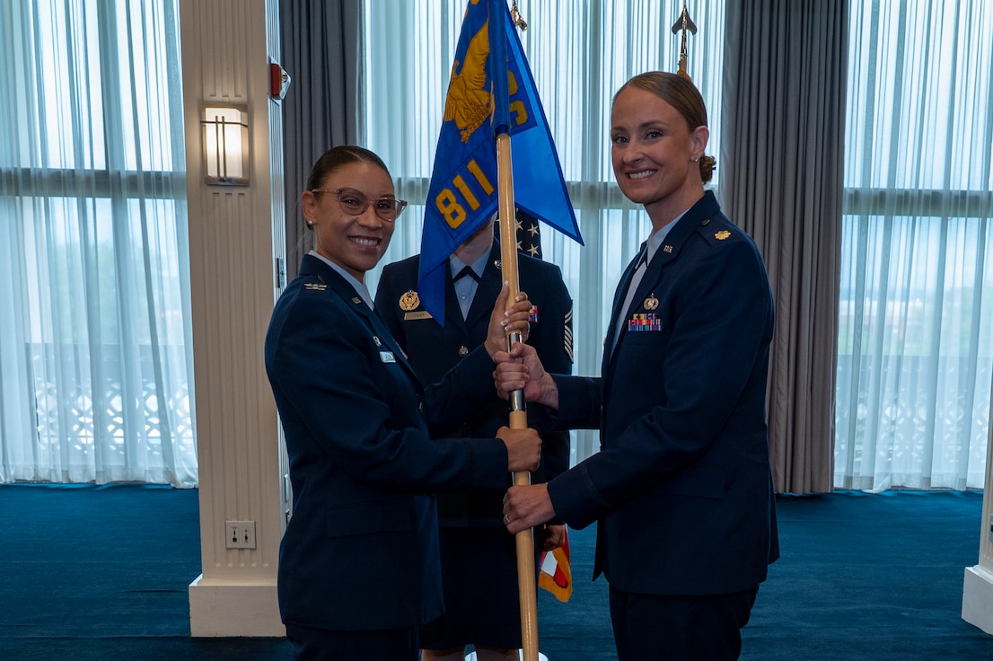 A photo of an Air Force Col. and Maj. holding a guidon together facing the  camera.