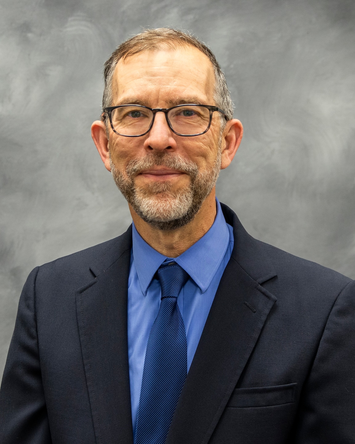 man in black suit jacket, blue shirt and tie smiling