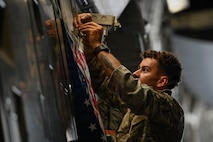 A photo of an Airman adhering a flag to a C-17 Globemaster III cargo plane