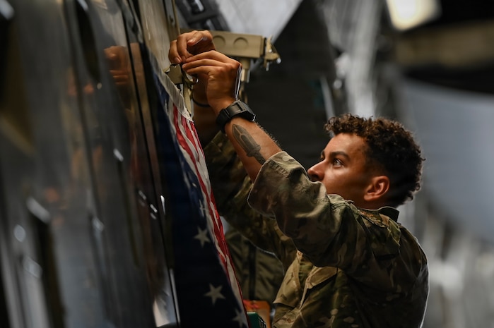 A photo of an Airman adhering a flag to a C-17 Globemaster III cargo plane