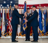 U.S. Air Force Maj. Gen. Ty Neuman, 8th Air Force and Joint-Global Strike Operations Center commander, left, relinquishes the guidon to U.S. Air Force Col. John Burrell, 5th Bomb Wing (BW) incoming commander, right, during a change of command ceremony at Minot Air Force Base, North Dakota, July 9, 2026. As the incoming commander, Burrell is responsible for leading the 5th BW’s B-52H Stratofortress operations and ensuring the wing remains ready to provide global strike capabilities in support of Air Force Global Strike Command’s strategic deterrence mission. (U.S. Air Force photo by Airman 1st class Anthony Ramey)