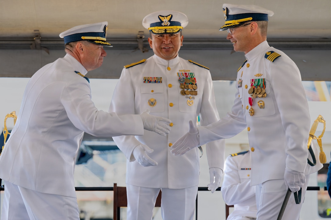 U.S. Coast Guard Capt. Michael Hunt (left), incoming commanding officer of Coast Guard Sector Puget Sound, shakes hands with Capt. Mark McDonnell (right), outgoing commanding officer of the sector, while Rear Adm. Arex Avanni (center), commander of the Coast Guard Northwest District, officiates during a change of command ceremony in Seattle, Washington, July 10, 2026