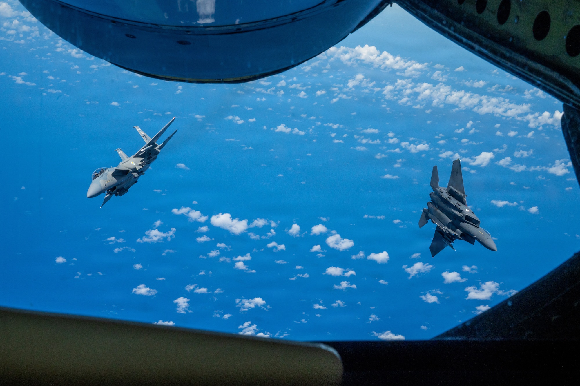 view of two fighter aircraft breaking away from each other outside of a refueling aircrafts boom pod window