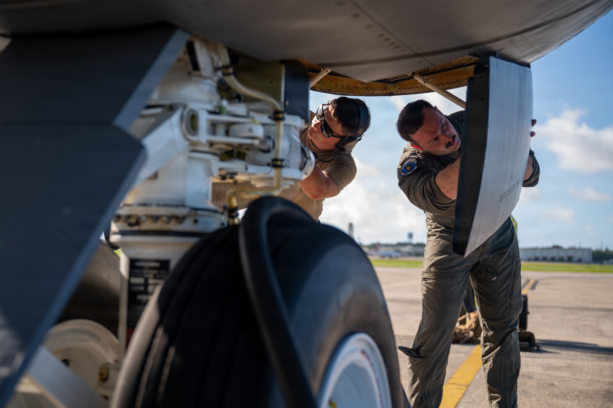 two military members look at an aircraft's front wheel hatch doors at the same time