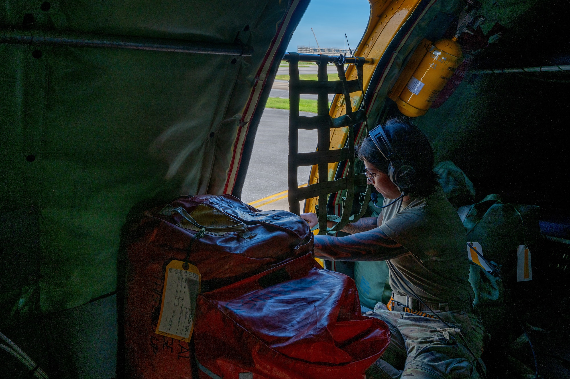 a military woman kneels in front of a aircraft door and attaches netting to it