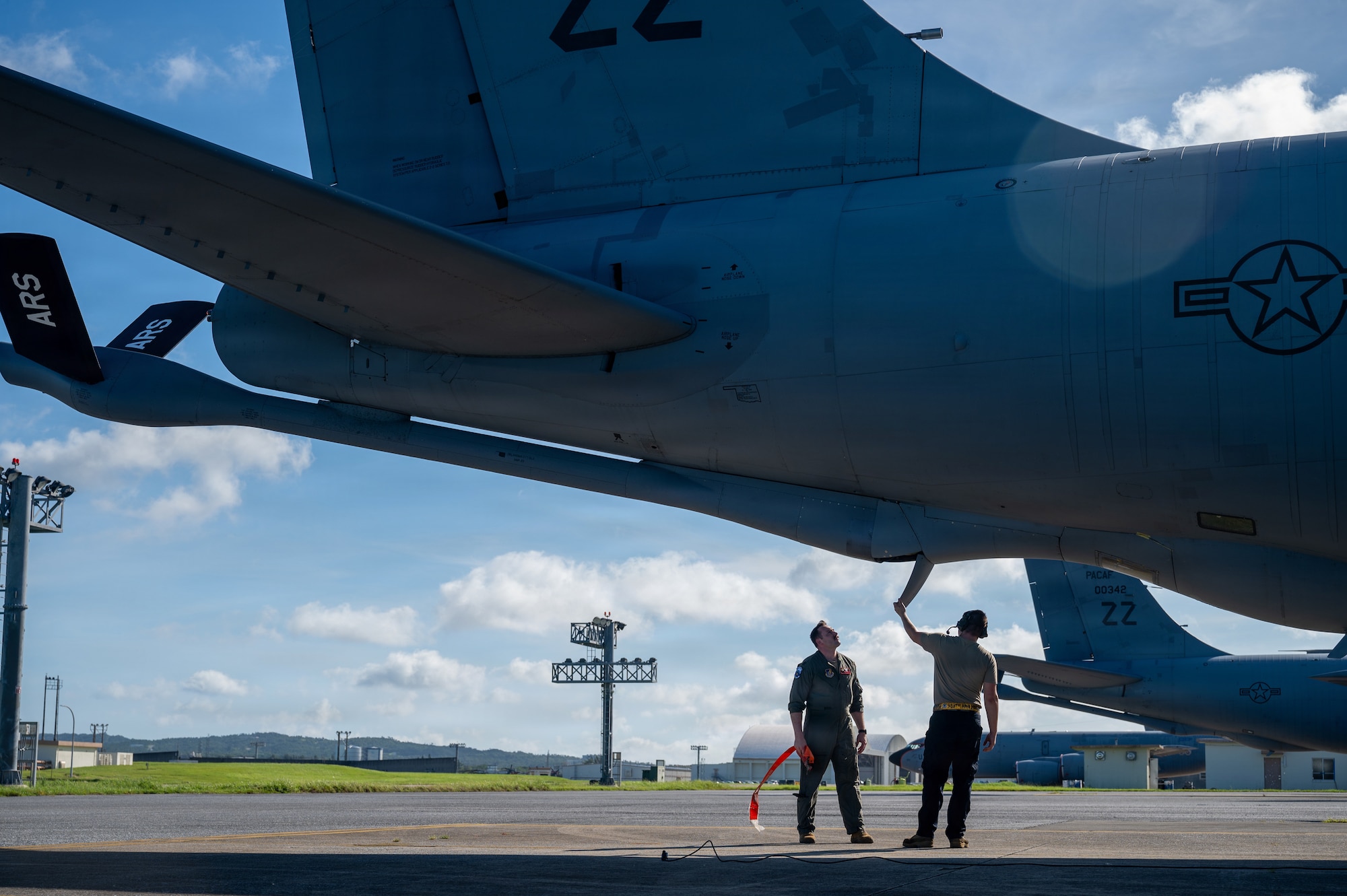 two military members look up at the boom pod from beneath the aircraft
