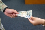 A 1,000 yen note is passed from a U.S. service member to a Japanese civilian at Yokota Air Base, Japan July 13, 2026.