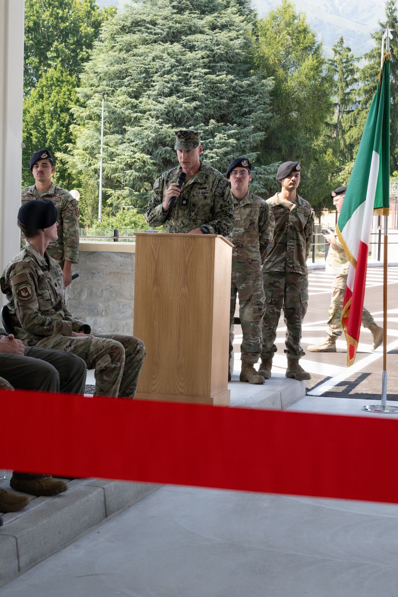 A Navy commander stands at a podium and speaks to Airmen at the opening of the new gate on Area 1.