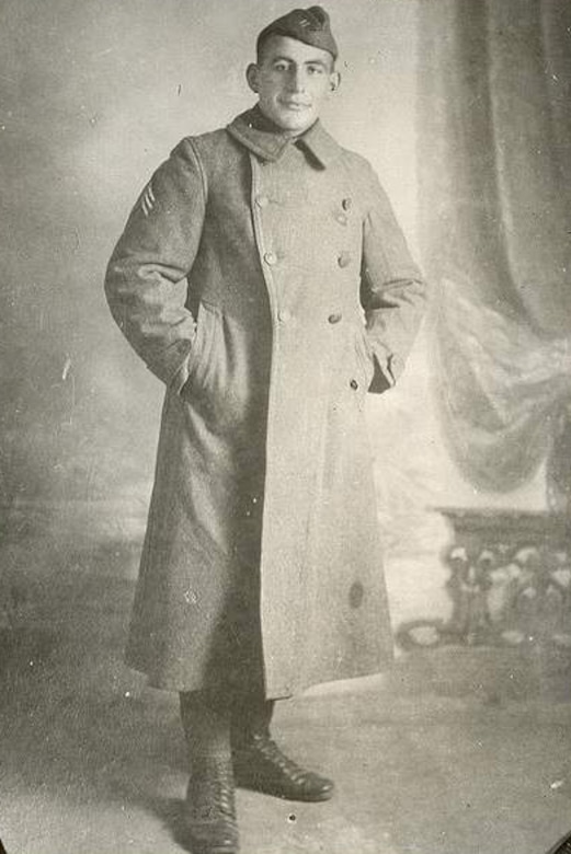 A black and white photo of a man in a military uniform posing with his hands in the pockets of his winter overcoat.