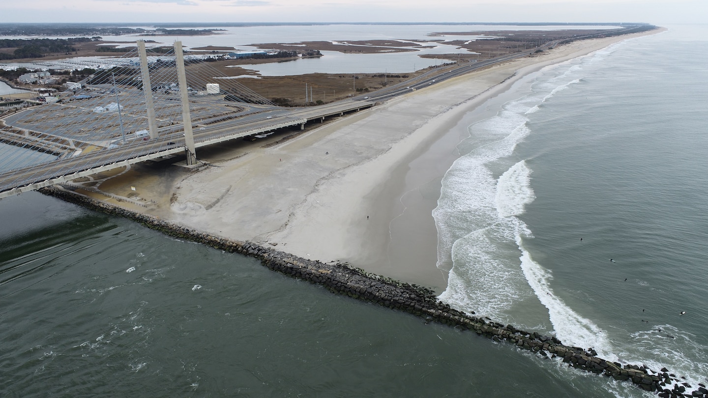 Photo shows a jetty structure along a coastline with a beach in the background