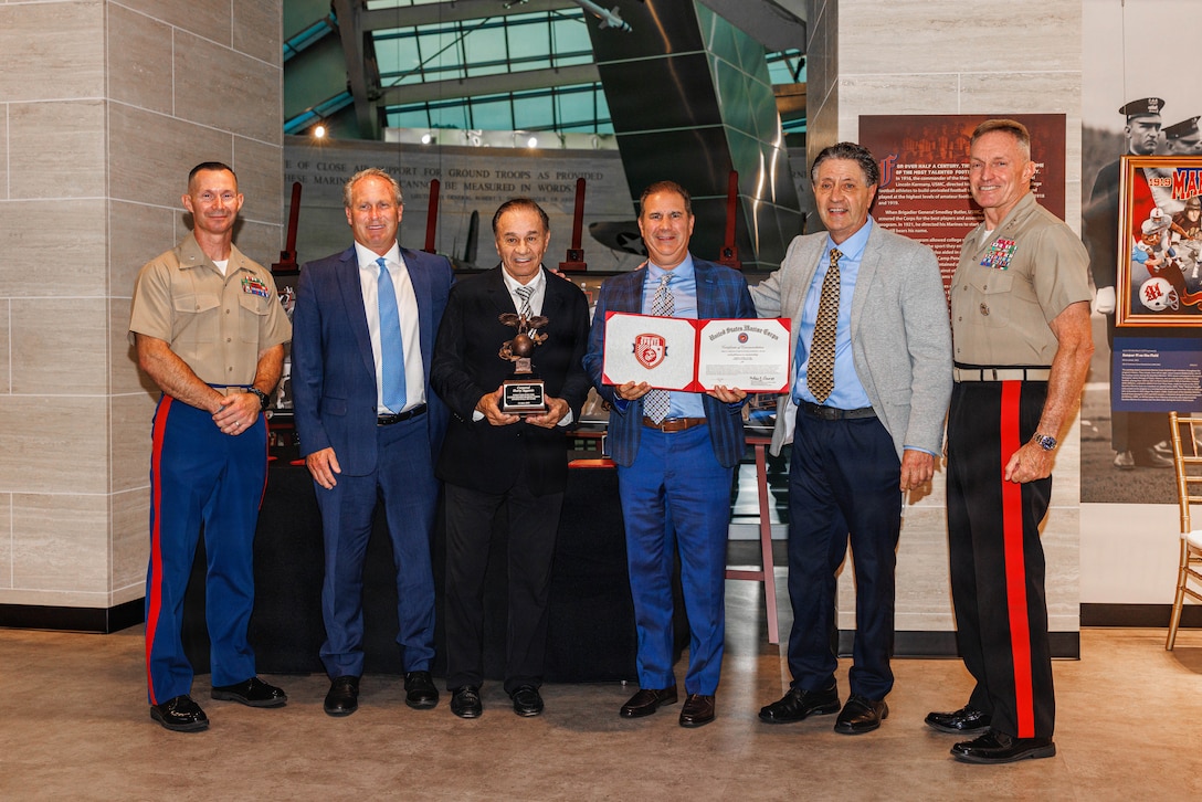 U.S. Marine Corps Lt. Col. Nathan Harmon, left, the branch head for officer program with Marine Crops recruiting command and U.S. Marine Corps Lt. Gen. William Bowers, the deputy commandant of manpower and reserve affairs, right, pose for a photo with Cpl. Agganis’ family during the 2026 Marine Corps Sports Hall of Fame Induction Ceremony at the National Museum of the Marine Corps in Triangle, Virginia, July 8, 2026. These Inductees were recognized for their athletic achievements and upholding the Marine Corps core values in and out of uniform. (U.S. Marine Corps photo by Lance Cpl. Donovan E. Melendez)