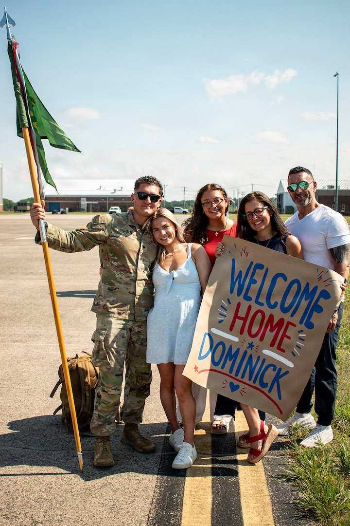 The guidon bearer for 643rd Military Police Company, Connecticut National Guard, poses for a photo with his family after returning from deployment at Bradley Air National Guard Base, East Granby, Connecticut, July 11, 2026.