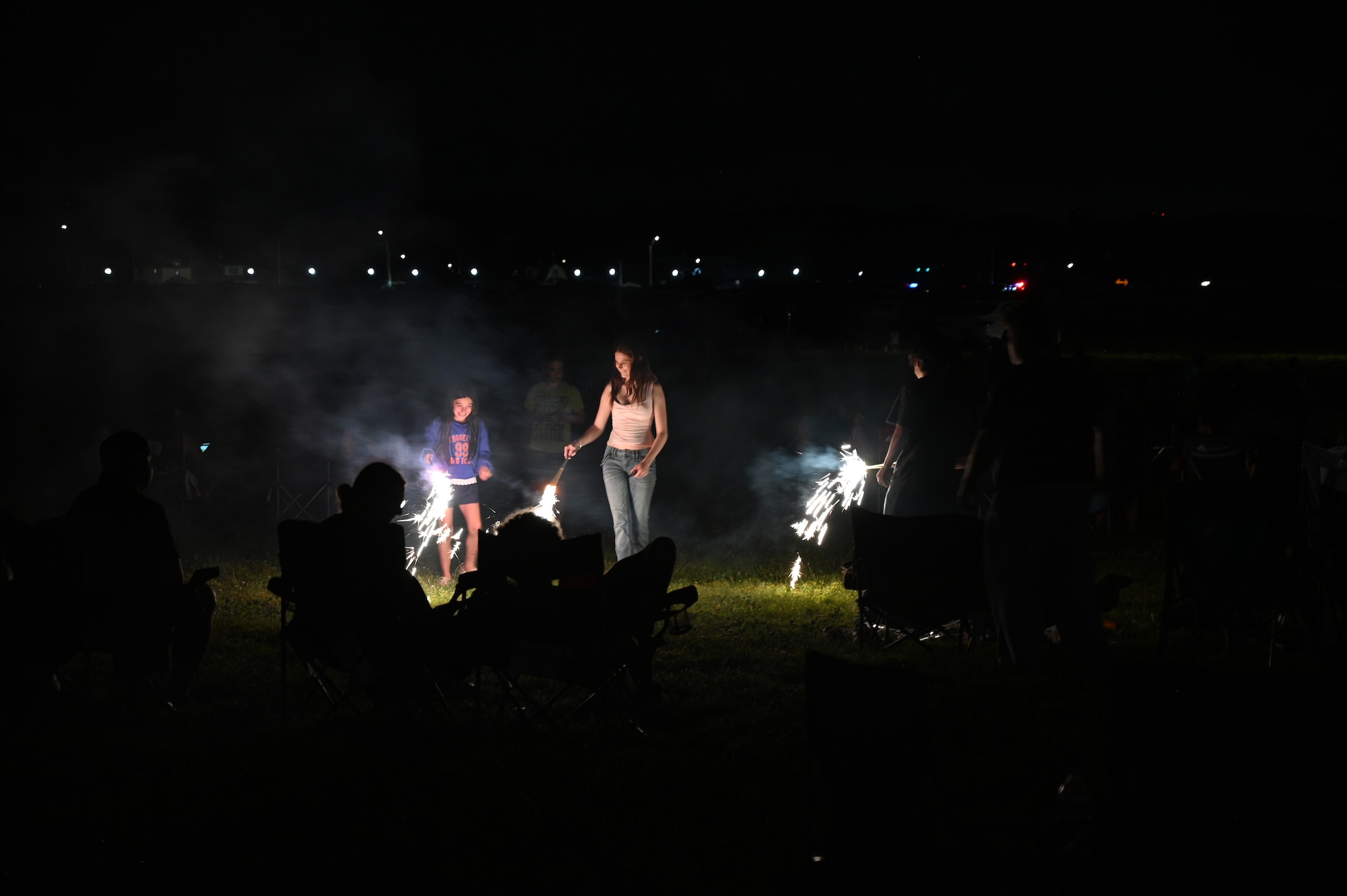 A family with sparklers awaits the drone show at dusk.
