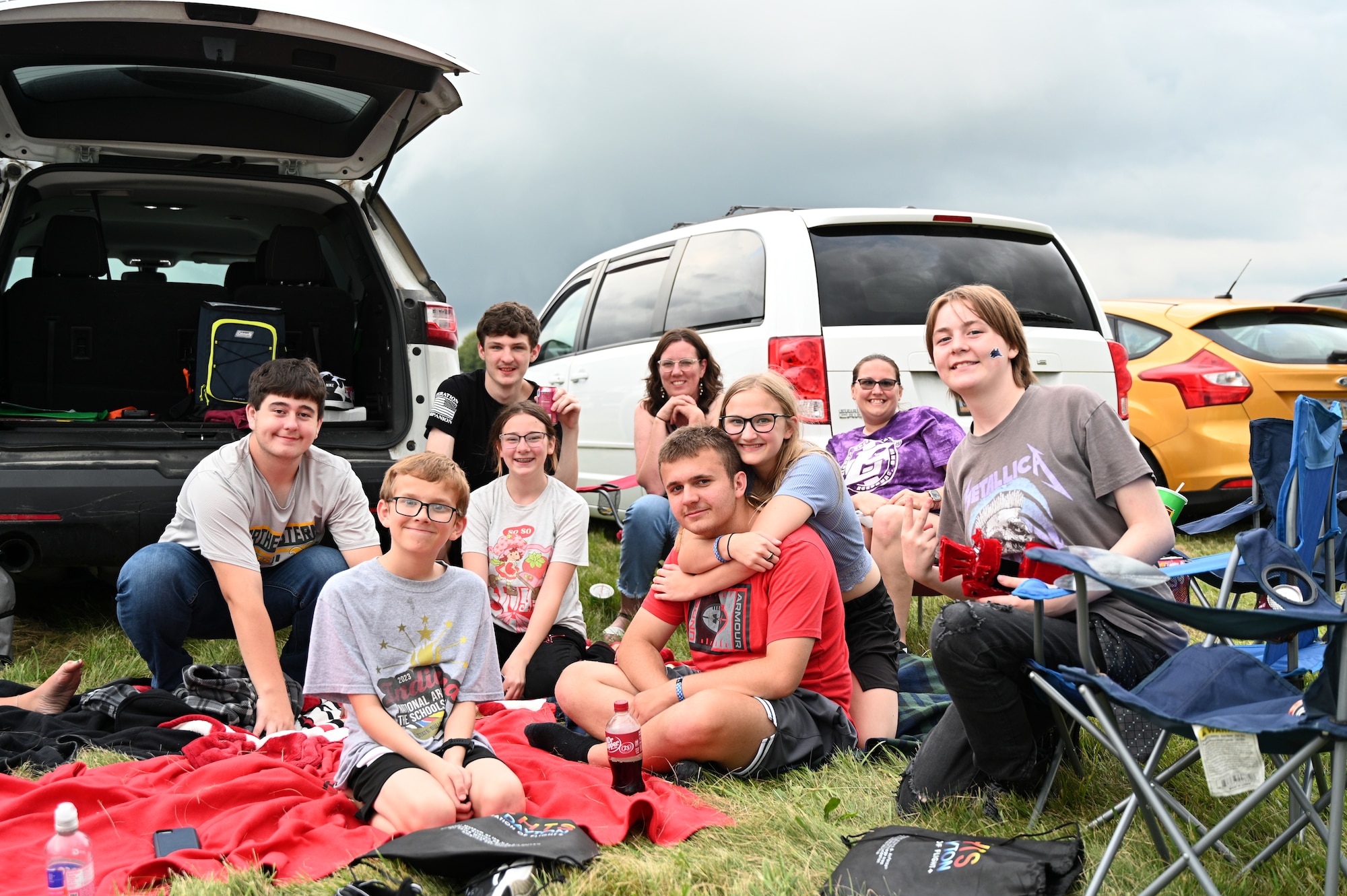 Family on the front lawn of the museum sitting on blankets and lawn chairs around the tailgate of their vehicle.